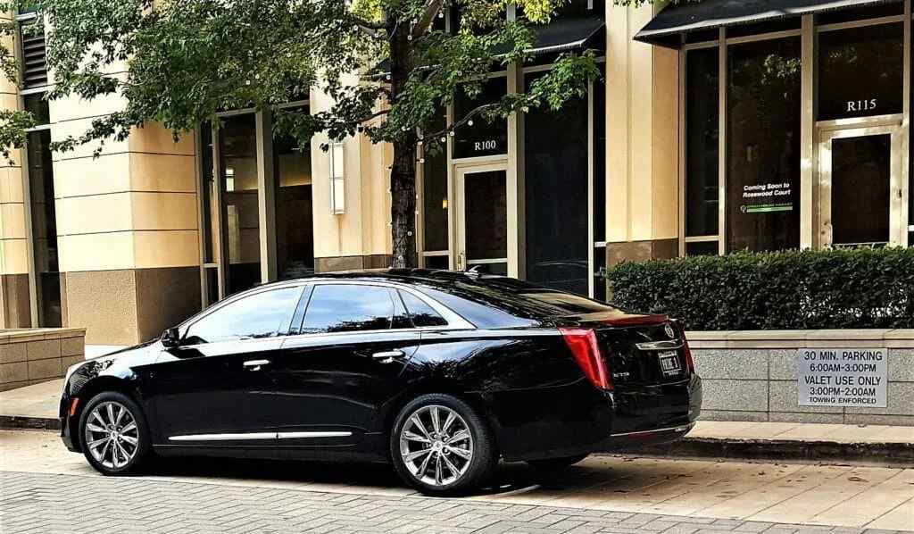 Black Cadillac XTS luxury sedan parked at a valet stand